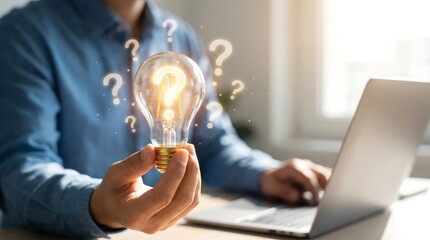 Man holding glowing light bulb with question marks around it, sitting at desk with laptop, symbolizing idea generation and problem solving