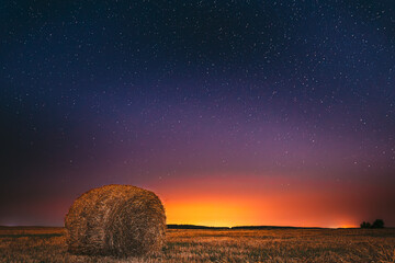 Night Starry Sky Above Field Meadow With Hay Bale After Harvest. Glowing Stars And Sunset Sunrise Lights Above Rural Landscape In August Month. Agricultural Colorful Background Copy Space © Great Brut Here