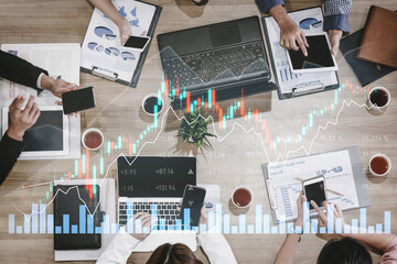 A team of professionals collaborates in an office setting, analyzing stock market trends using laptops and smartphones, surrounded by data charts and financial documents. Scalp