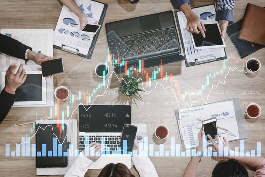 A team of professionals collaborates in an office setting, analyzing stock market trends using laptops and smartphones, surrounded by data charts and financial documents. Scalp - Powered by Adobe