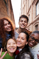Fototapeta premium Group of multiethnic student friends taking a selfie together outdoors at university. Diverse people having fun using phone to take photos for social media. Vertical image with copy space.