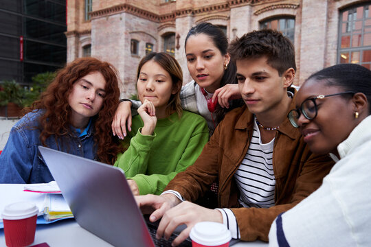 Multiracial group of students gathering to study at university campus, concentrated looking at a laptop together, working on a school project as a teamwork. Copy space.