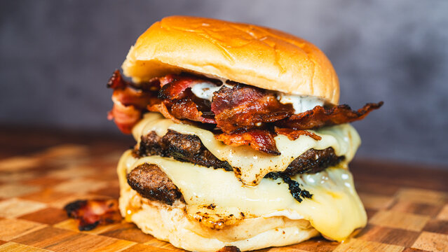 Delicious double deck bacon cheeseburger on a beautiful wooden board. Juicy patties, crispy bacon, melted cheese. Ultimate indulgent comfort food presentation.