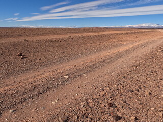 Dirt road in the desert under a blue sky with layered clouds