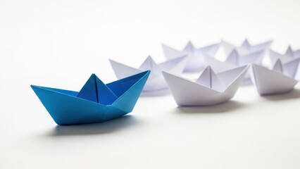 Blue paper boat leads a fleet of white origami boats on a white surface