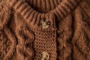 Close-up of brown knitted wool cotton sweater. Details of cozy winter or fall children's sweater, buttoned cardigan, pullover. Neckline detail, sleeves, large knit pattern. Trendy Color 2025