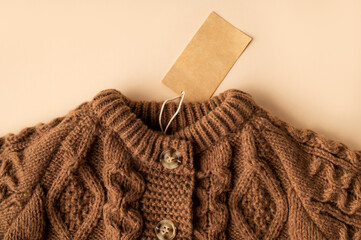 Paper cardboard tag on brown knitted wool sweater, pullover or cardigan with buttons on beige background. Children's clothing mockup, blank label for logo application. Stylish clothes fashion, cozy