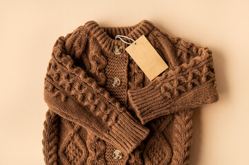 Paper cardboard tag on brown knitted wool sweater, pullover or cardigan with buttons on beige background. Children's clothing mockup, blank label for logo application. Stylish clothes fashion, cozy