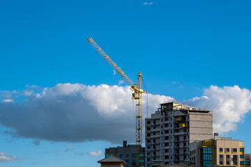 Fototapeta premium Tower Crane and Apartment Building Under Construction Against Cloudy Sky