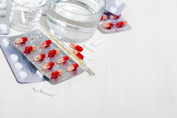 thermometer and a glass of water, medicines in tablets and capsules, top view