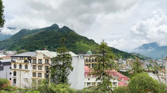 A panoramic panning shot from a hotel balcony, showcasing the beauty of buildings nestled among lush green mountains and misty clouds. Captured in Sa Pa, Lao Cai, Vietnam on August 24, 2024