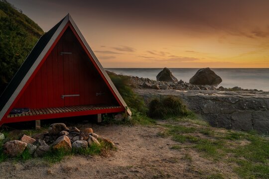 small red wooden A-frame bothy and fireplace on the north coast of Bornholm island at sunset