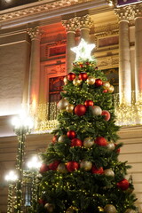 Beautiful decorated Christmas tree with red and golden balls in front of elegant historic building in center of Bucharest