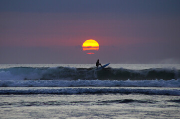 Silhouette of surfer in the waves at the sunset
