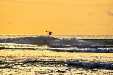 Silhouette of surfer in the waves at the sunset