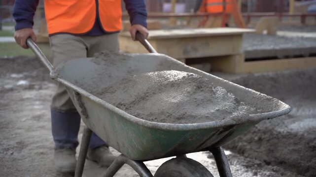 Construction worker transporting concrete using wheelbarrow