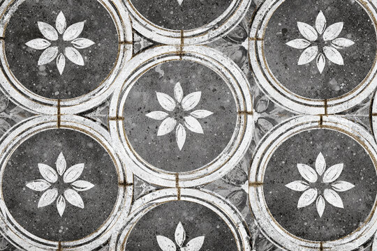 detailed close up of old grey stone floor tiles with white floral patterns and golden accents