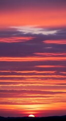 Fototapeta premium A vibrant sunset paints the sky with fiery hues. Streaks of color traverse the heavens, from deep purple to blazing orange, over a darkened silhouette