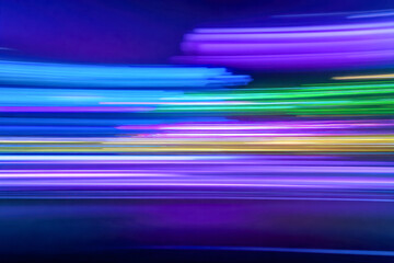 Vibrant neon light trails in blue, purple, green, and yellow creating a dynamic abstract motion effect against a dark background at night