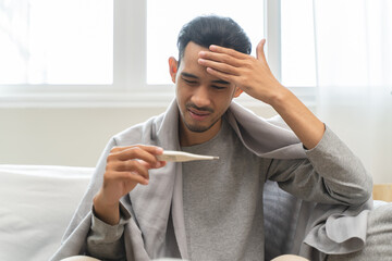 Seasonal cold sickness in people concept, Sick asian man looking at thermometer during measuring...