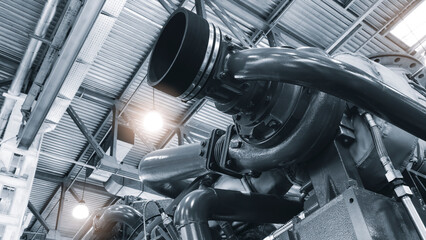 Large  piston gas engine electric generator with many valves and pipes. The engine is orange and has many valves.