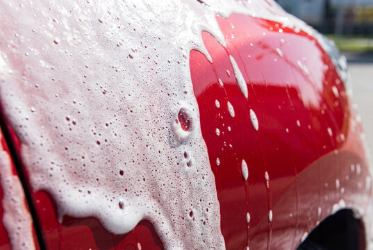 Close-up of red car body covered with white soap foam during car wash
