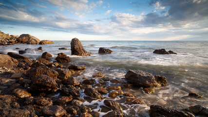 Beautiful sunset seascape with a rocky shore, sunset sky over the sea horizon, sky with soft clouds, sea with waves crashing against the rocks, Crimea, South Coast