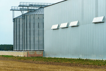 A large modern plant located near a wheat field for the storage and processing of grain crops. view of the granary illuminated by the light of the setting sun against the blue sky. harvest season.