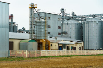 A large modern plant located near a wheat field for the storage and processing of grain crops. view of the granary illuminated by the light of the setting sun against the blue sky. harvest season.
