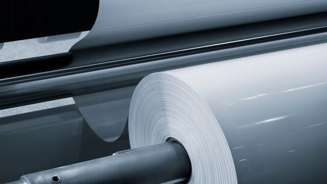 Large industrial automatic machine for cutting and gluing PVC film on wood chipboard and MDF boards for furniture production, rollers with white PVC film are loaded