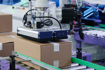 robotic arm places cardboard box on conveyor belt at distribution warehouse for storage or delivery of an online order or mail shipment. Modern technologies, logistics, storage, delivery concept