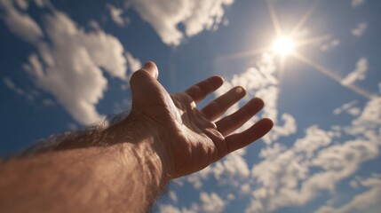 Human hand reaching for bright sun in blue sky with clouds.