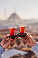 A woman's and a man's hands holding glasses of Turkish tea