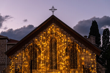 A small church in Haifa lit up for Christmaschher against the sky at twilight time.
