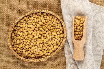 Fototapeta premium Raw soybeans with kitchen utensils on jute cloth, close-up, top view.