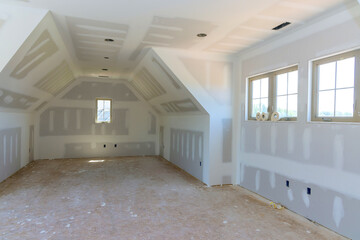 Spacious room with unfinished drywall bare floors, awaiting interior finishing touches in newly built house.