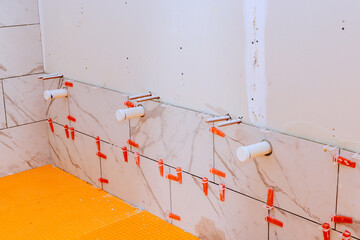 Workers are laying tiles on bathroom wall, preparing plumbing fixtures for installation in home...