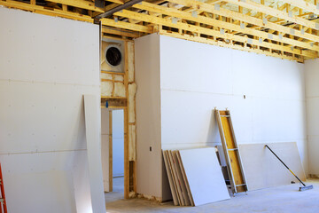 Drywall installation underway in spacious construction site with wooden beams exposed.