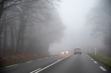 Driving car in thick fog with poor visibility, winter forest on hills, heavy fog and humidity,...