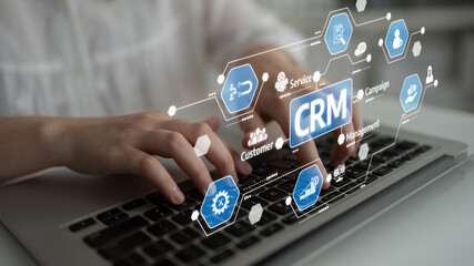 Close-up view of hands typing on a laptop with a digital overlay of CRM icons, symbolizing customer management and modern business solutions in a digital workspace. Tessel
