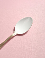 A spoon covered in yogurt on a pastel pink background