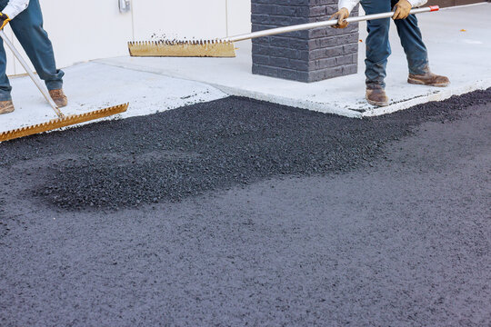 Construction workers spread hot asphalt on pavement near building road maintenance.