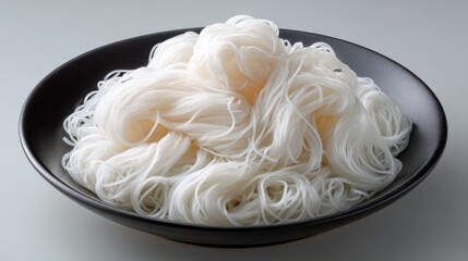 A bowl of white noodles sits on a black plate