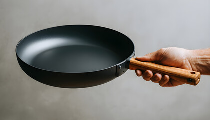 A person is holding a pan with a wooden handle. The pan is black and has a shiny surface