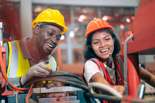 Two happy factory workers team African American man black woman engineer checking machine manufacturing plant Industrial safety helmet heavy industry teamwork production maintenance mechanic gear vest