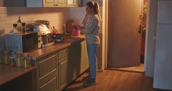 A young woman in casual clothes dries her wet hands with paper towels in a bright, modern kitchen in the evening. Everyday routine, lifestyle.