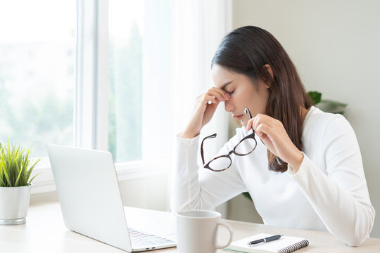 Eye problem concept, fatigue asian young woman tired eyes, irritated rubbing nose, relief vision pain after work on laptop computer, eye strain, hand holding glasses, suffer migraine, bad blurry.