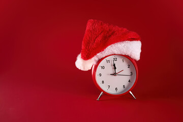 Festive Time. A red clock adorned with a Santa hat against a vibrant red background.