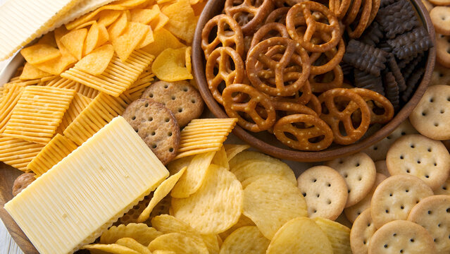 A high-angle, close-up photograph showcases an assortment of snack foods arranged to fill the frame. The composition is a mix of textures and shapes, creating a visually appealing arrangement. The sna
