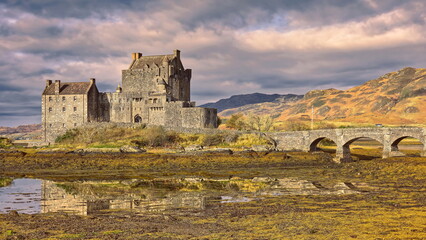 Sunny moment on a cloudy day lighting Eilean Donan tidal island-castle at low tide, linked to the mainland by a stone footbridge. Dornie-Scotland-189